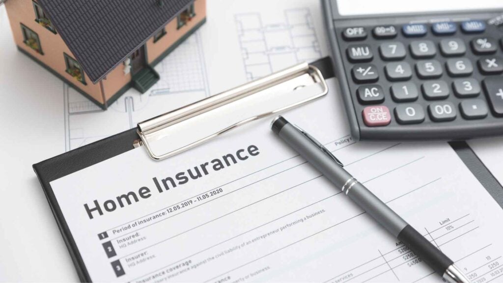 Home insurance policy clipboard with house model, blueprints, calculator, and pen